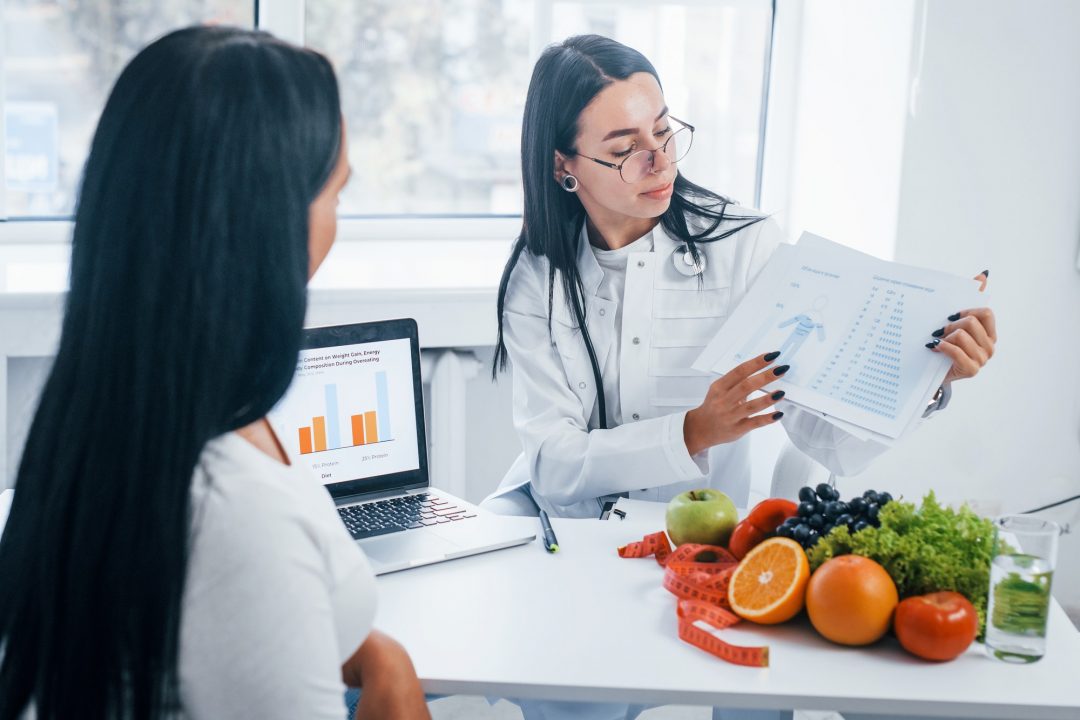 female nutritionist with laptop gives consultation to patient indoors in the office